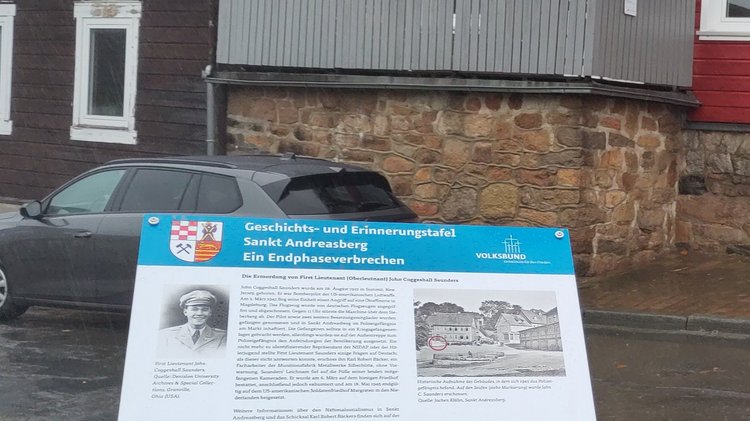 Pulttafel mit Text und Bildern vor einem Gebäude