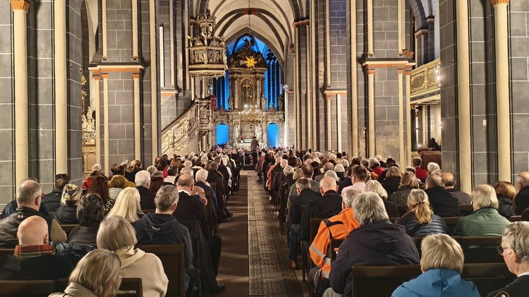 Eine große Gruppe Menschen in einer Kirche. Von hinten aufgenommen, vorne der Altar.