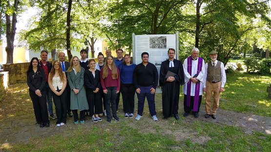Eine Gruppe junger und älterer Menschen, die vor einer Tafel mit Text und Bildern stehen.