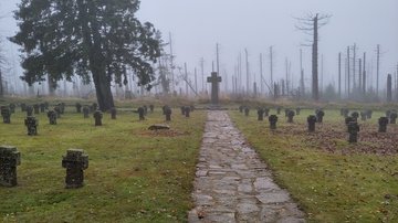 Mittig ein steinerner Weg. Links und rechts auf Rausenflächen Grabkreuze. Hinten, mittig ein Hochkreuz.