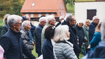 Eine Gruppe Menschen von der Seite fotografiert. Im Hintergrund zwei Gebäude.