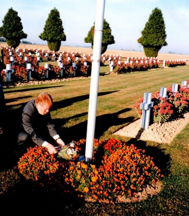 Ein Mann legt gebückt Blumen nieder. Im Hintergrund viele weiße Grabkreuze.